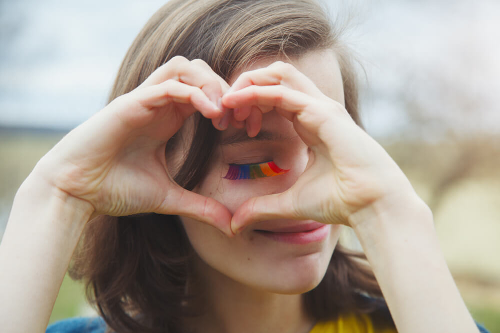 A sweet short hair girl wearing rainbow mascara doing a heart gesture