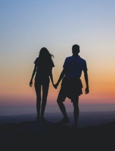 Paar, das auf einem Hügel steht und sich gemeinsam einen Sonnenuntergang ansieht. 
