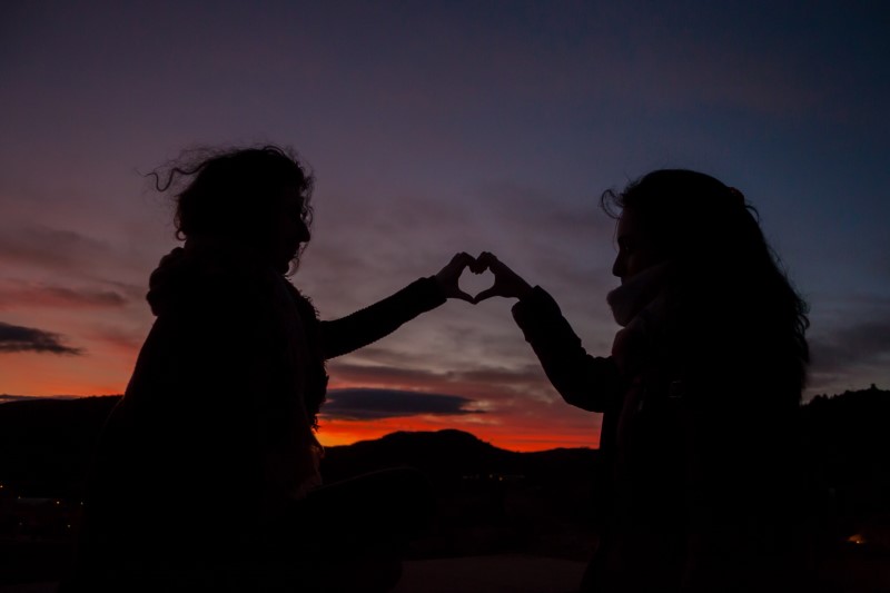 zwei Menschen, die im Sonnenuntergang mit ihren Händen ein Herz bilden